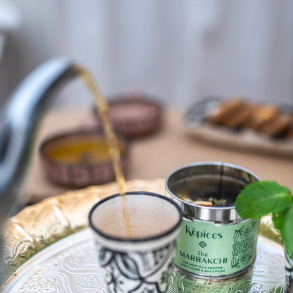 Bocal ouvert de thé vert marocain Képices à côté d'un verre, théière versant le thé à la menthe, cannelle et safran