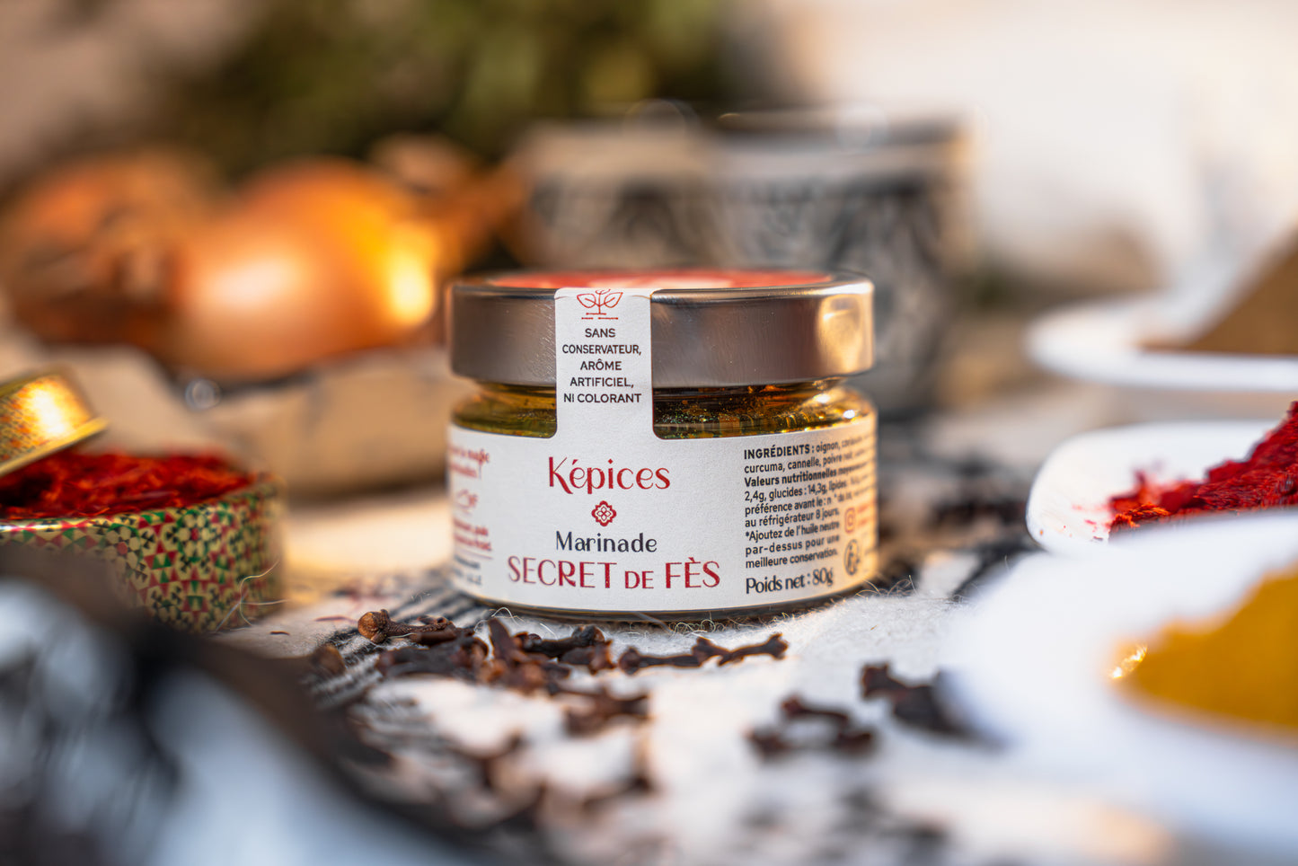 Pot de Marinade Secret de Fès Képices entouré de clous de girofle, paprika et herbes séchées.