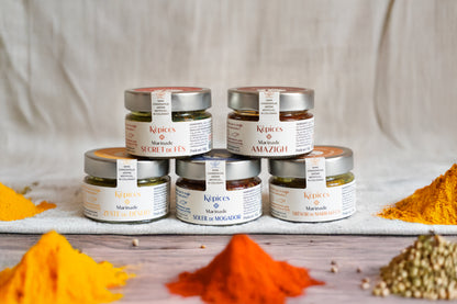 Coffret Découverte Képices avec cinq marinades marocaines artisanales – Amazigh, Zeste du Désert, Trésor de Marrakech, Secret de Fès et Soleil de Mogador – entourées d’épices colorées.