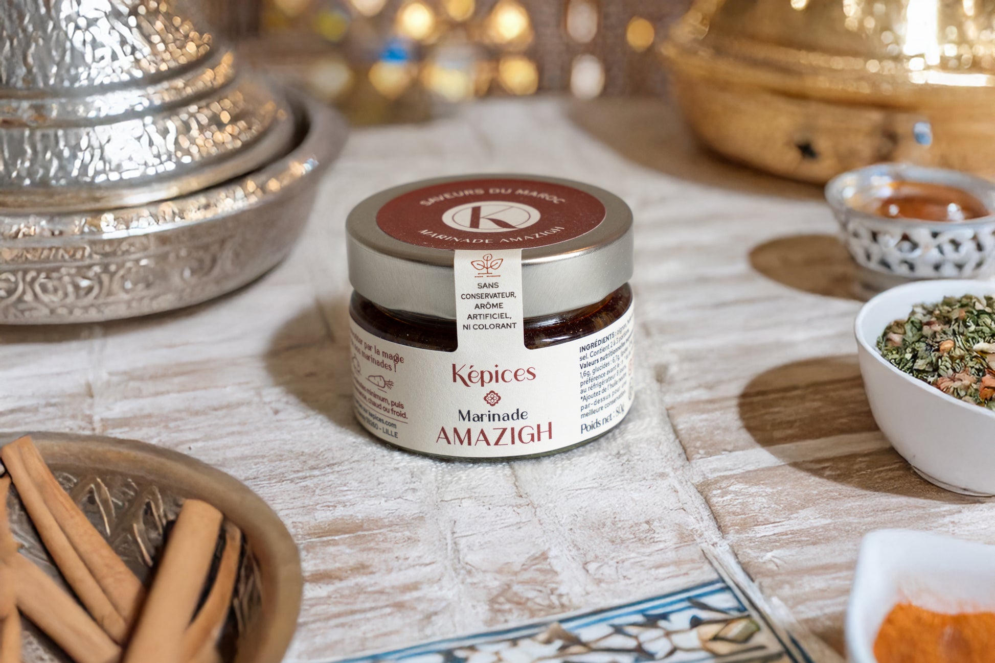 Pot de Marinade Amazigh Képices sur table orientale, accompagné de cannelle, coriandre et paprika.