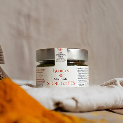 Pot de Marinade Secret de Fès Képices entouré d’épices marocaines colorées, safran, curcuma et oignons.