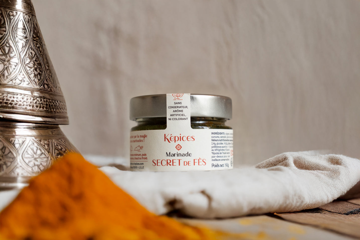 Pot de Marinade Secret de Fès Képices entouré d’épices marocaines colorées, safran, curcuma et oignons.