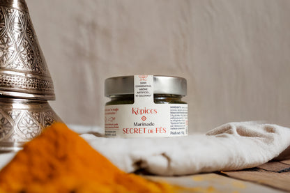 Pot de Marinade Secret de Fès Képices entouré d’épices marocaines colorées, safran, curcuma et oignons.