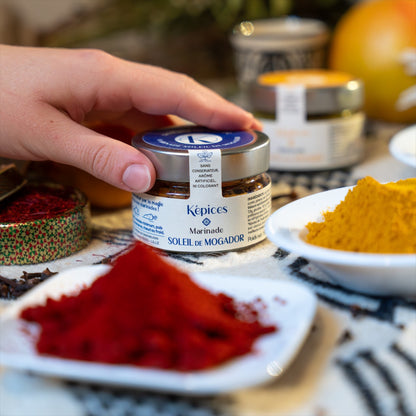 Présentation de la marinade marocaine Soleil de Mogador Képices sur une table avec des épices et des herbes fraîches