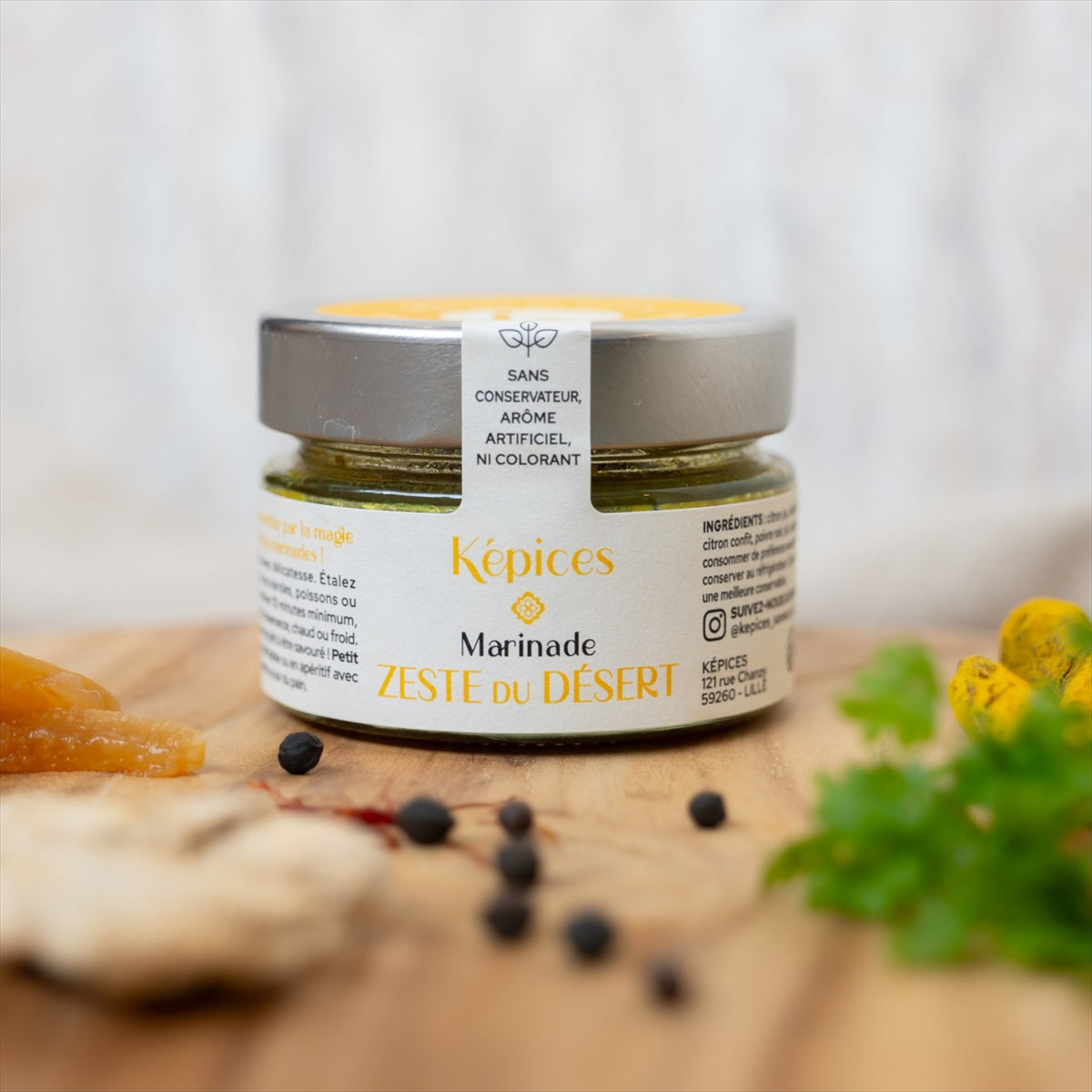 Pot de Marinade Zeste du Désert Képices sur planche en bois avec citron confit, gingembre et herbes fraîches.